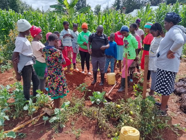 Heimkinder stehen um Pflanzloch auf einem Feld