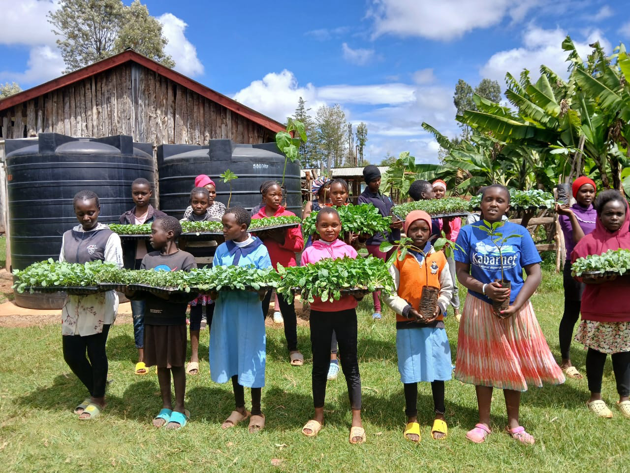 Orphans with seedlings in front of the new water tanks